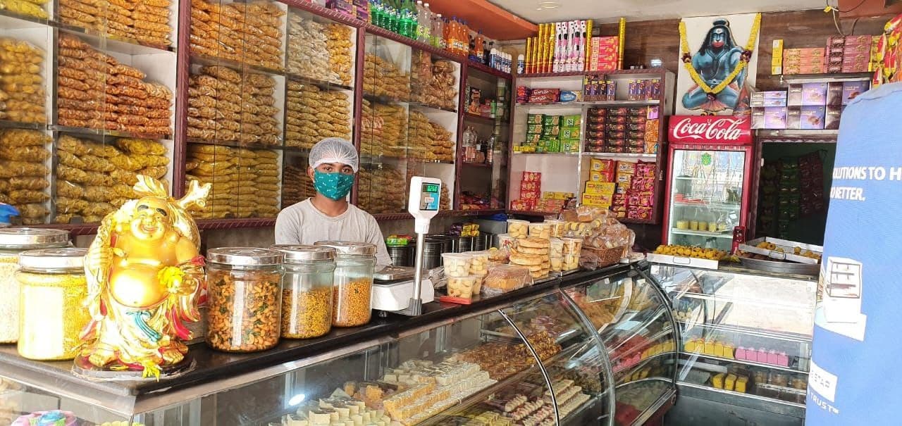 Inside our sweet shop — glass counter, shelves of sweets and snacks, and our team in G. Mamidada.